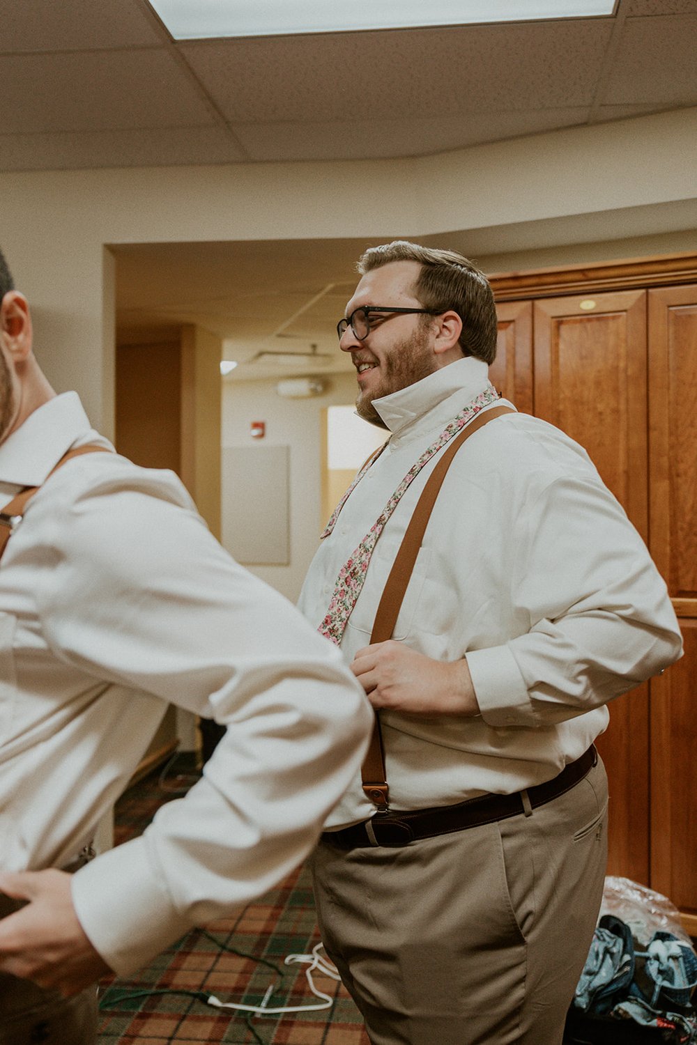 Groomsmen stands holding his suspenders while getting ready for the wedding. 