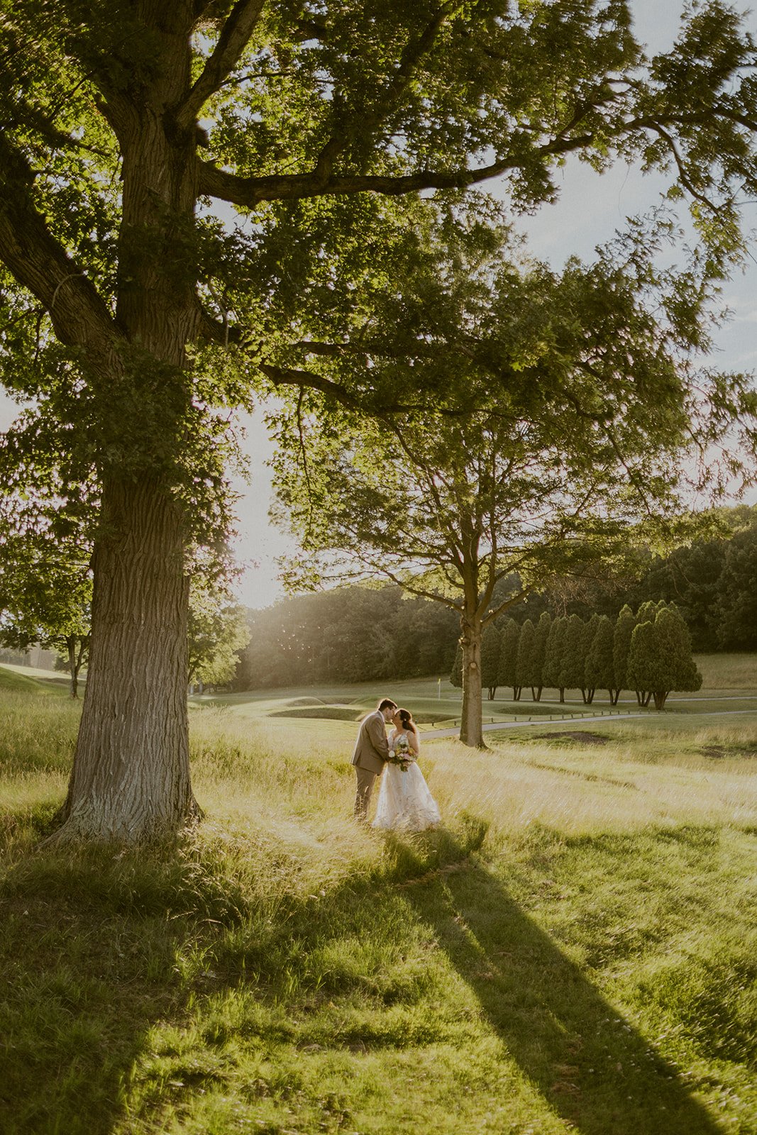 Bride and groom share a kiss by a tree during the golden hour.