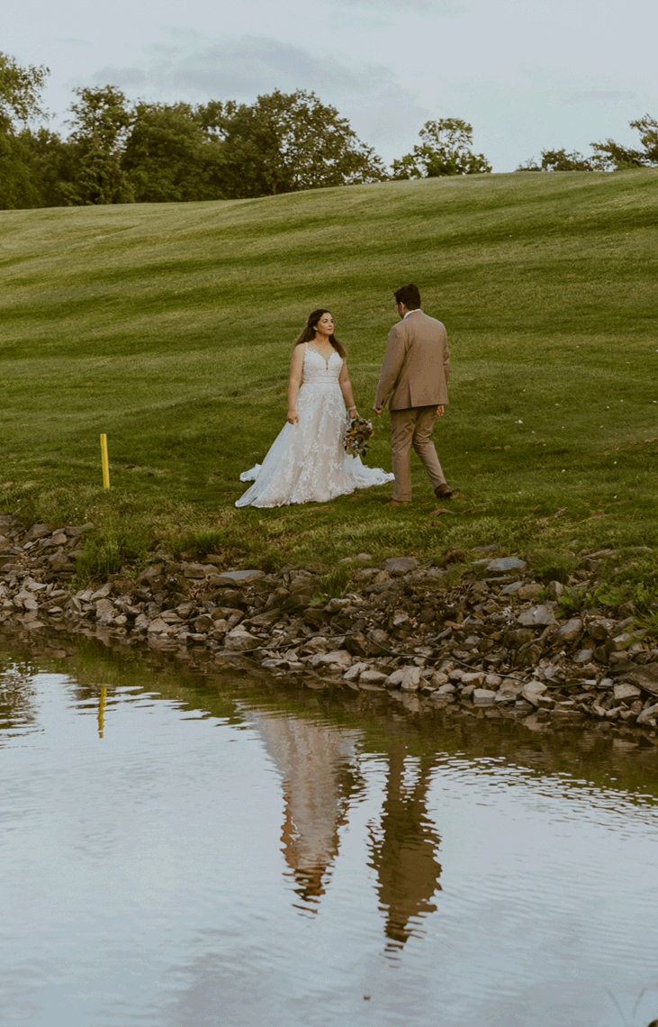 Bride and groom walk to each other by the pond while sneaking a kiss.