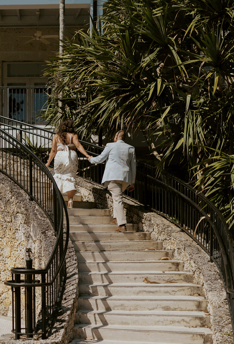 The couple holding hands walking up the stone stairs of the Fairchild Botanic Gardens.