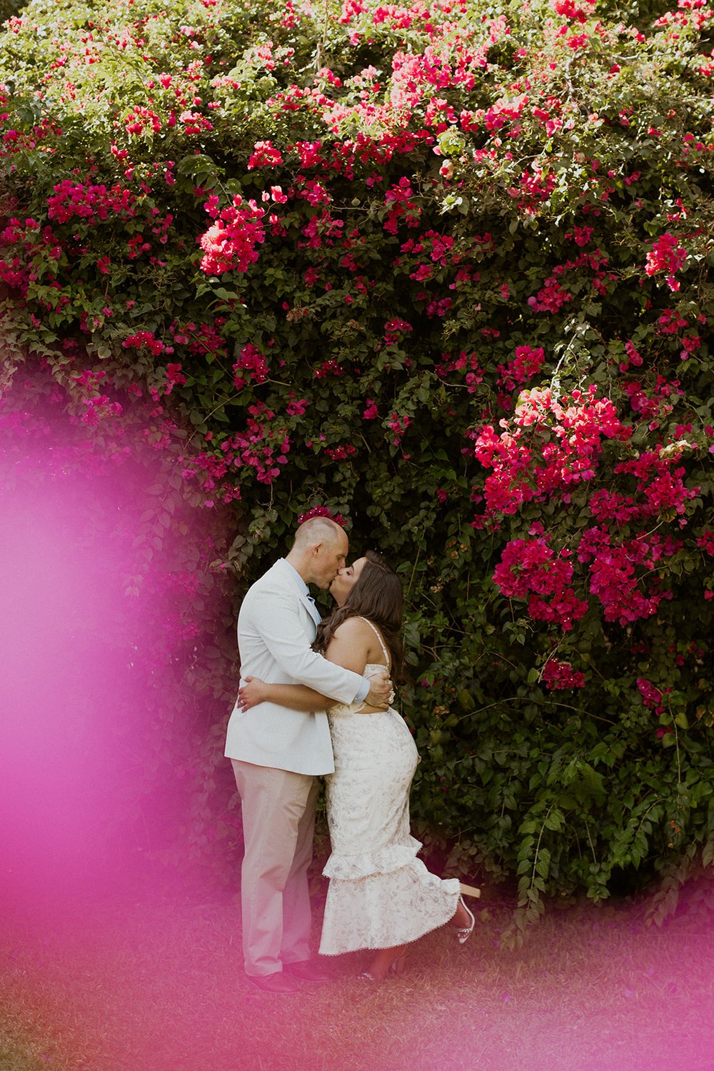 Gigi steals a kiss from her groom while hiding in lush pink florals. 