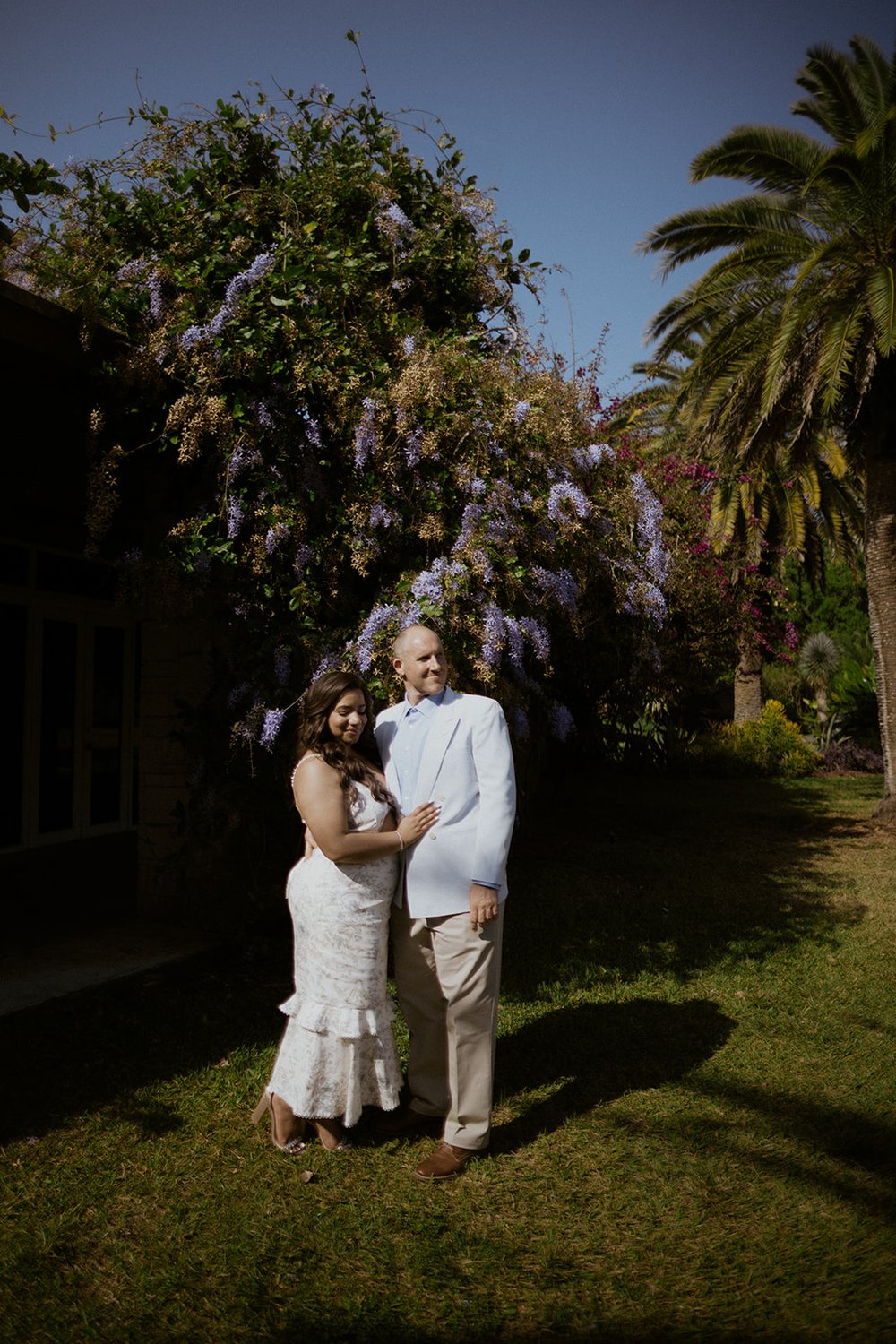 The couple standing by a lilac tree looking at the botanical gardens. 