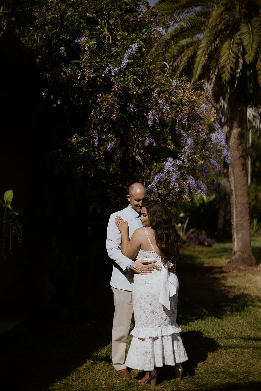 The couple holding one another close standing by a lilac tree. 