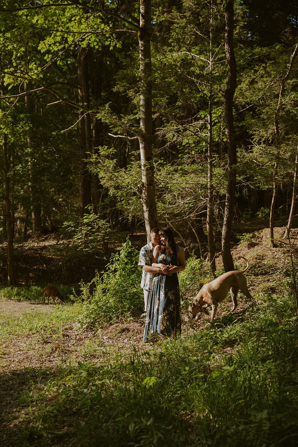 Hade holds maggie while standing in the lush greenery of the falls while their dogs wander. 