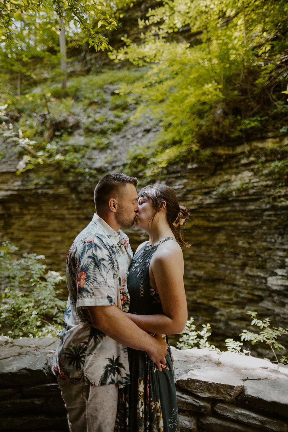 Maggie kisses her future groom with the view of lush greenery growing off the rocks of the falls. 