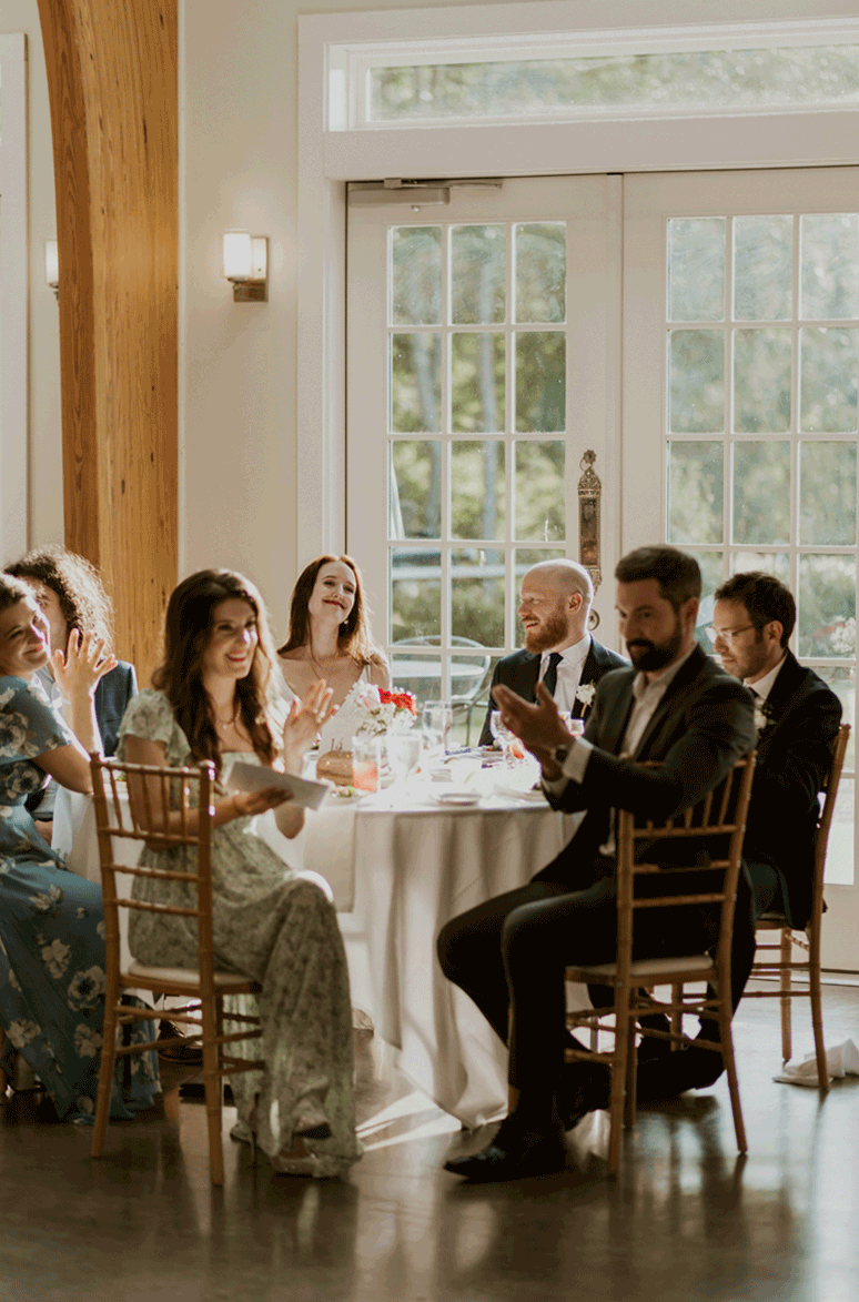 Bridal party sits together clapping during the speeches of the wedding.