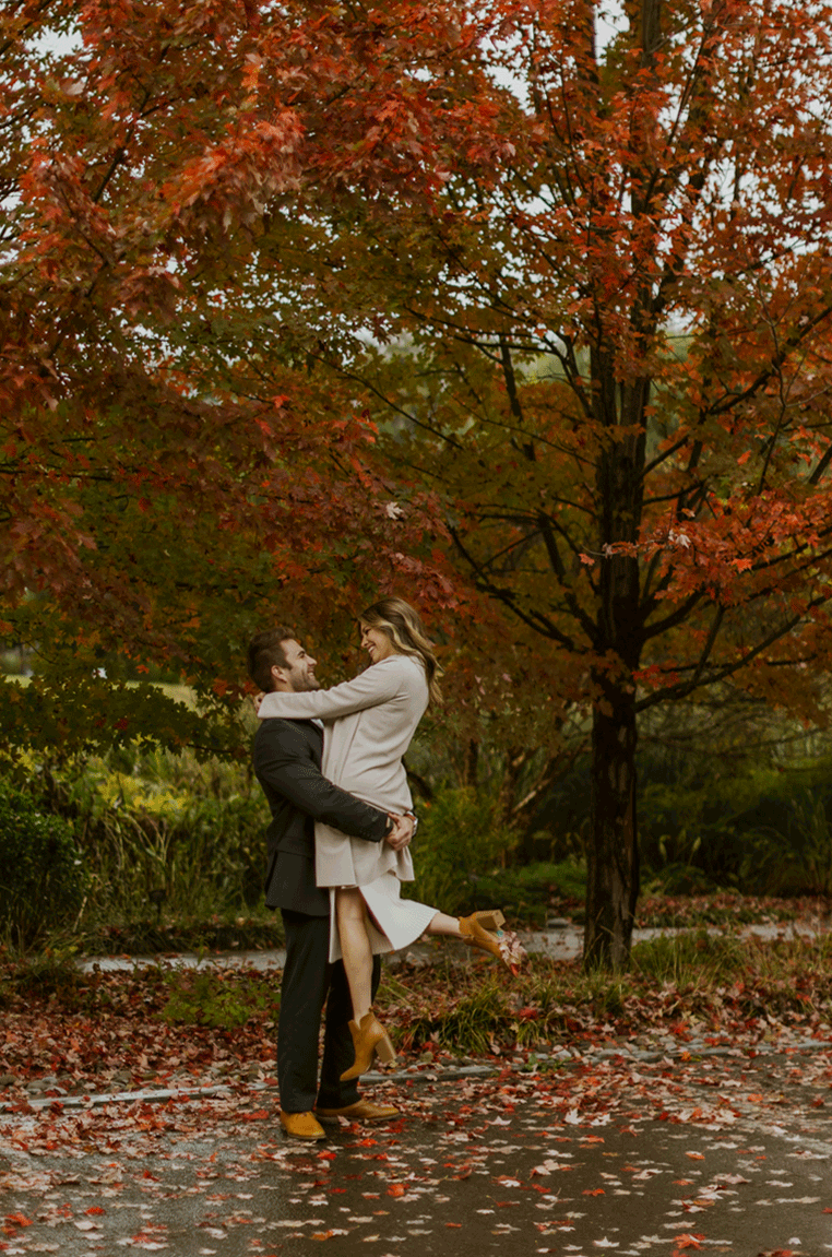  The brides future husband spins her in circles with smiles and laughter under a beautiful fall tree.  