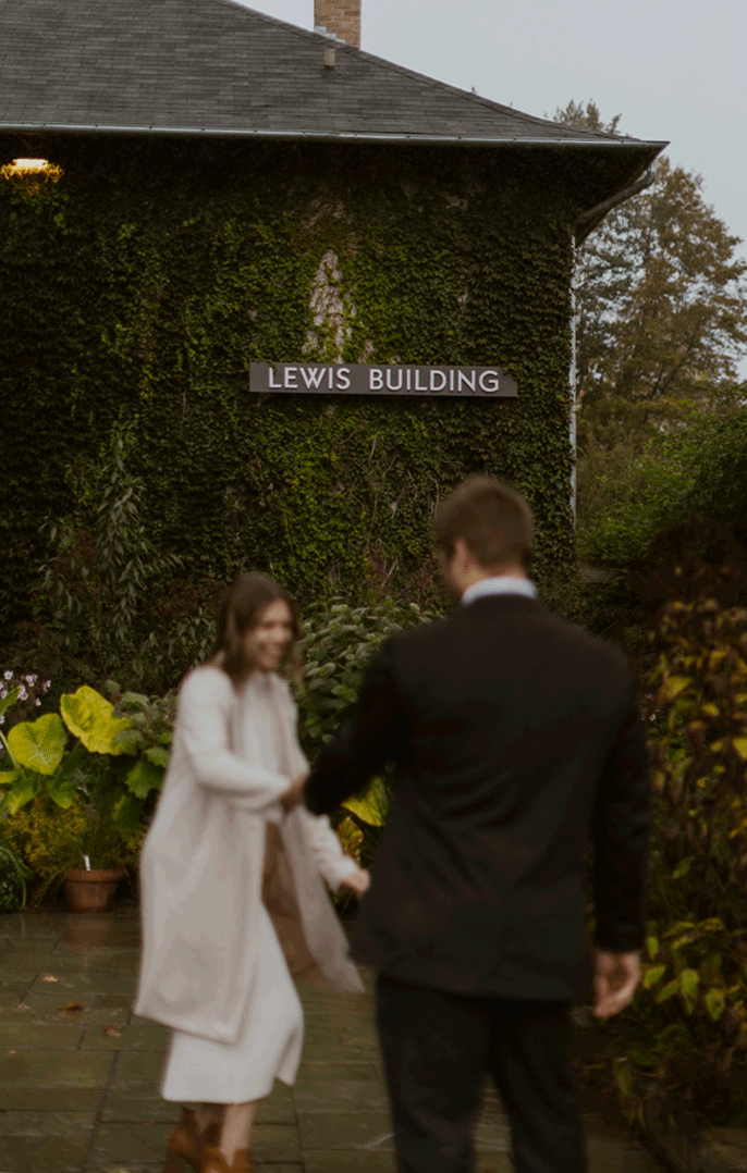  The future bride grabs her groom by the hand walking him to the Lewis building. Surrounded by greenery and ivy. 