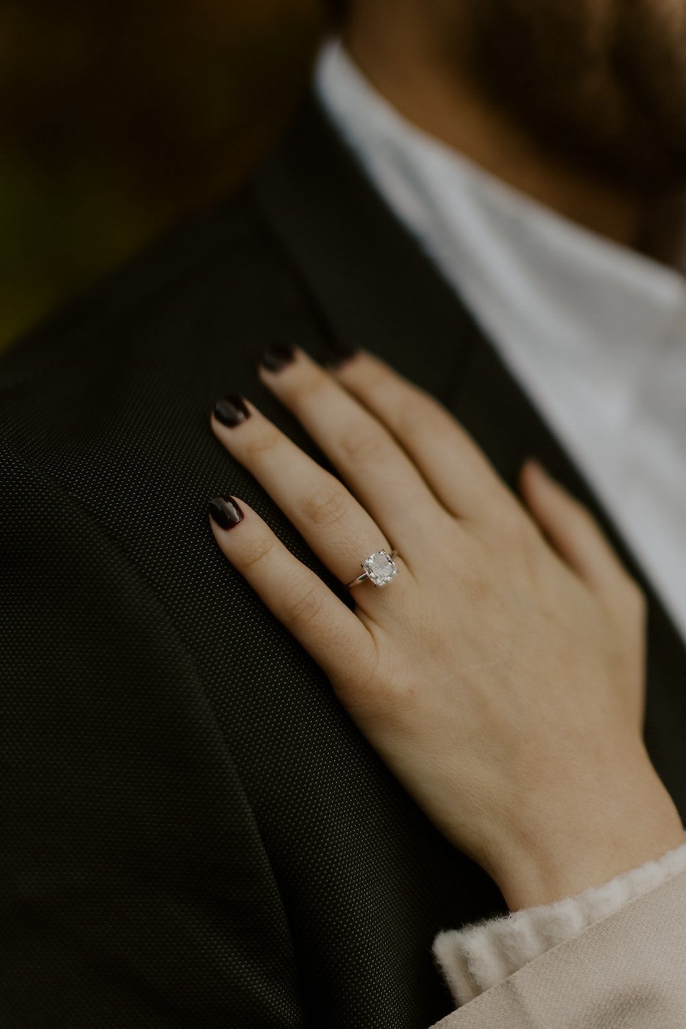  Close up view of the engagement ring. The future bride touches her grooms chest.  