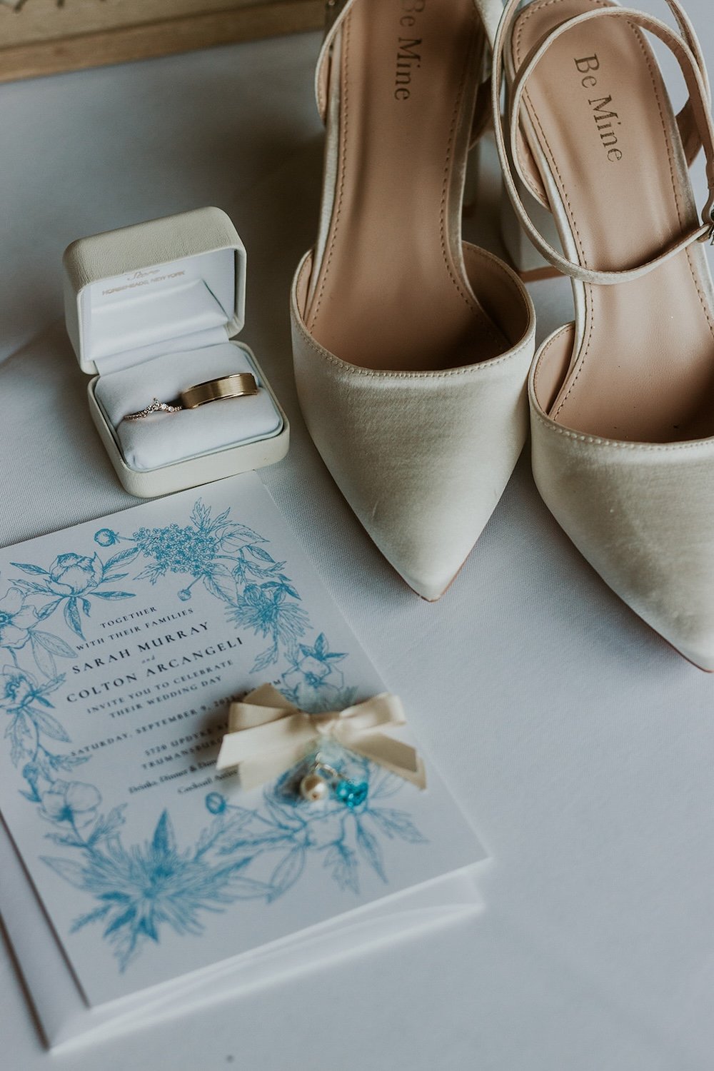 Detail photo of the brides closed toe champagne heels, their engagement rings and wedding stationary.