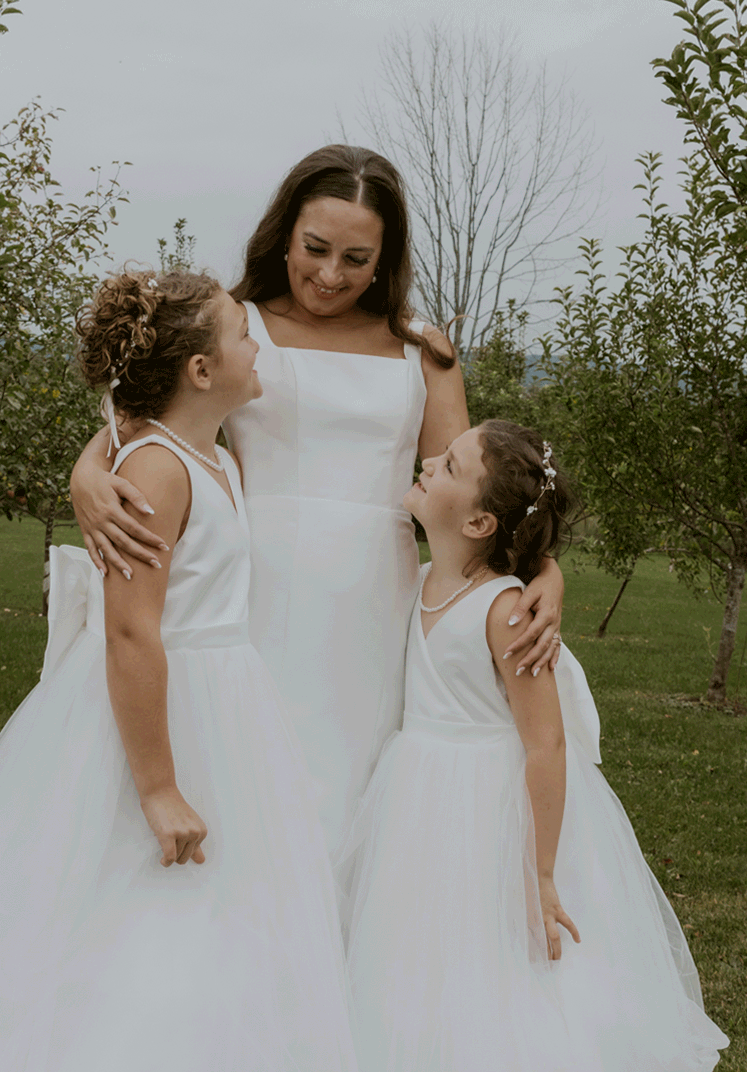 The bride holds her flower girls close while sharing a smile.