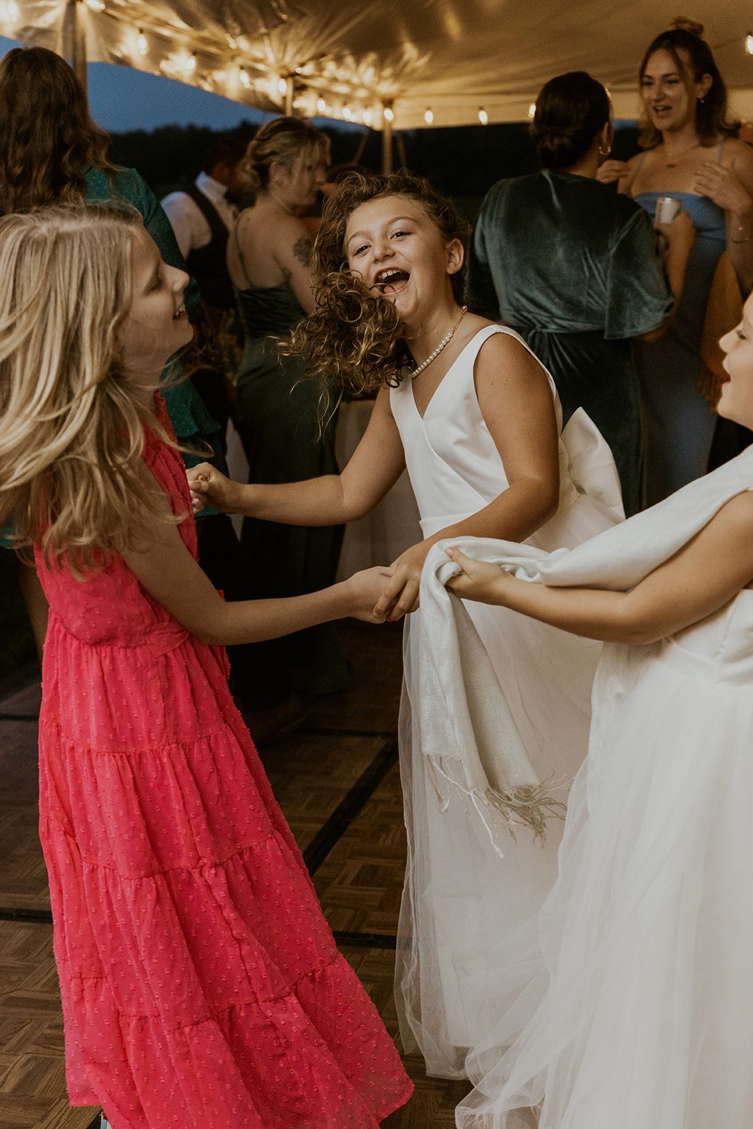 The flower girls dance happily with other children at the wedding. 