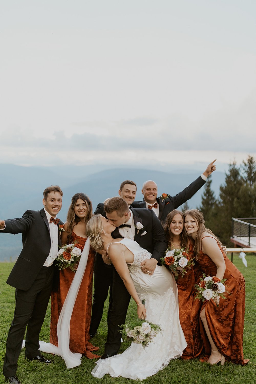 The groom dips his new wife as he kisses her. The bridal party stand behind them cheering them on. 