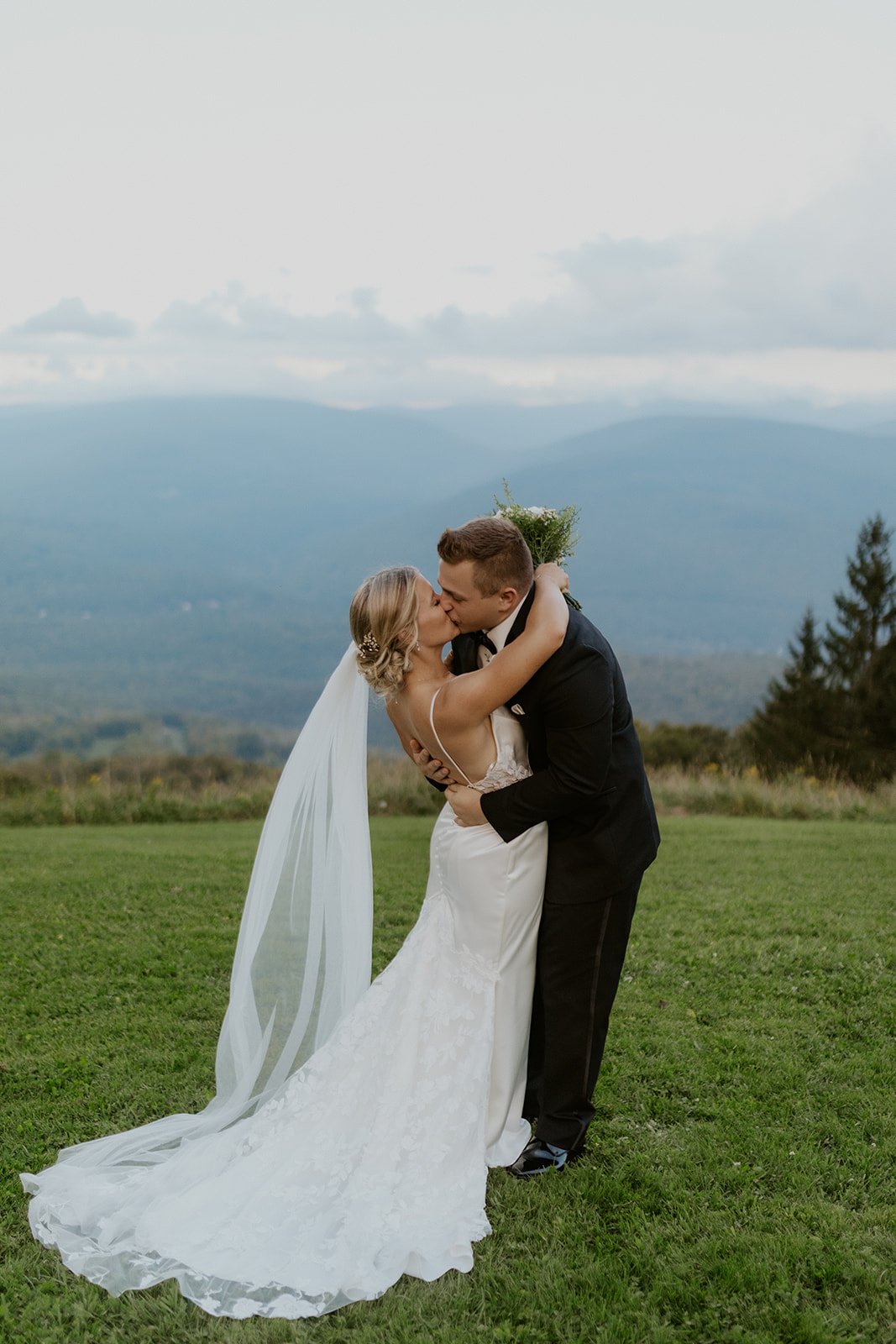 The bride and groom steal a kiss at the top of the mountain. The brides veil flows in the wind. 