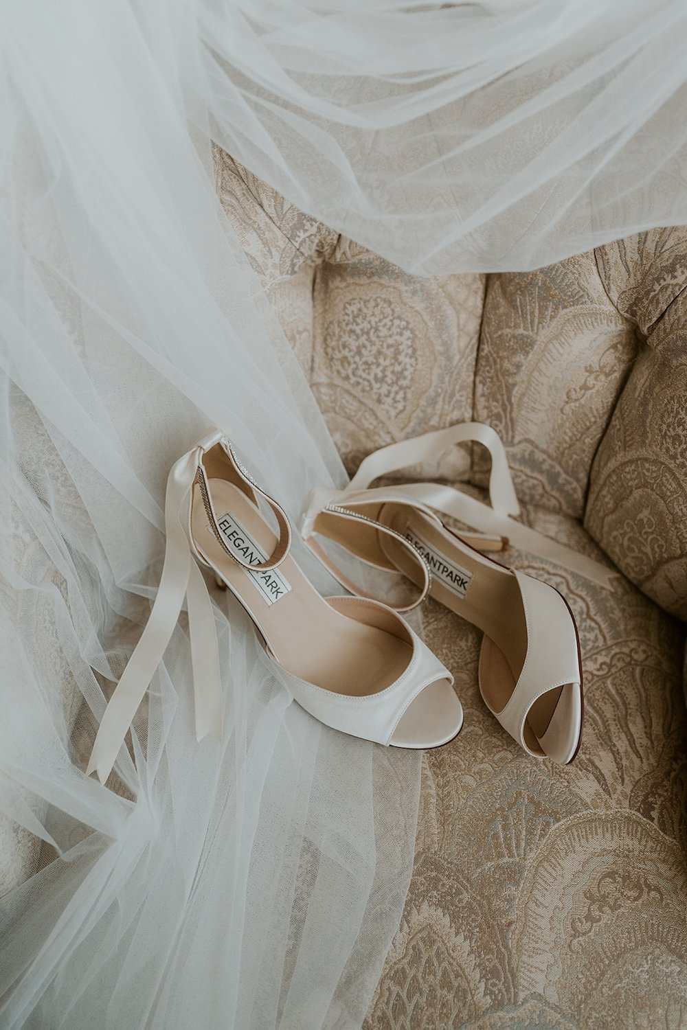 The brides heels resting on the chair with the veil decorated around them.