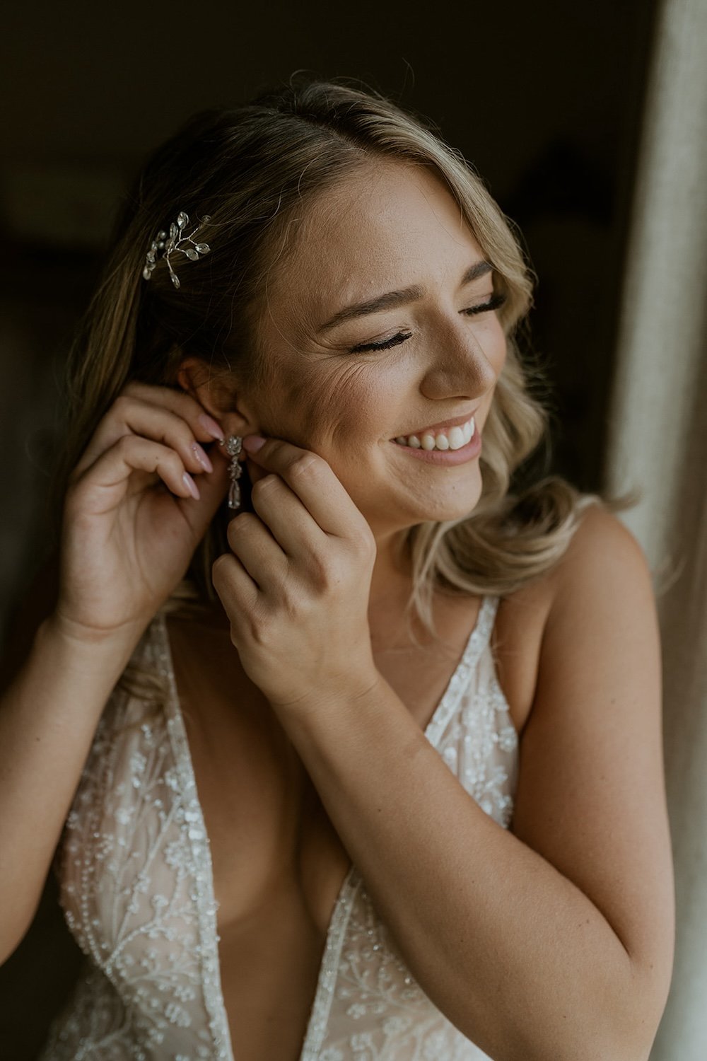 The bride smiles happily as she puts her bridal jewelry on.