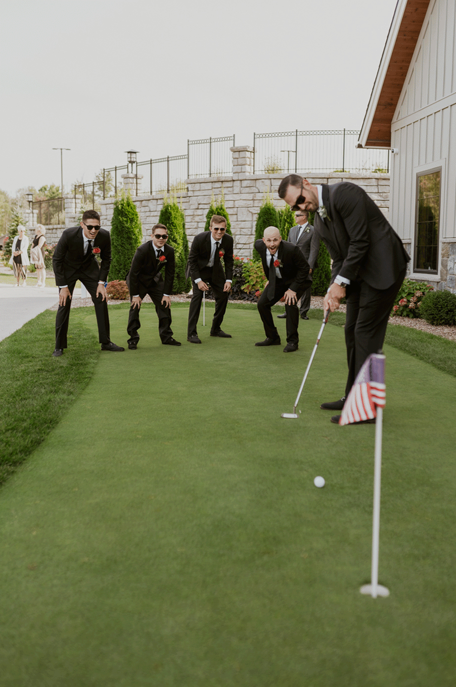 The groomsmen cheer on the groom as he attempts a putt.