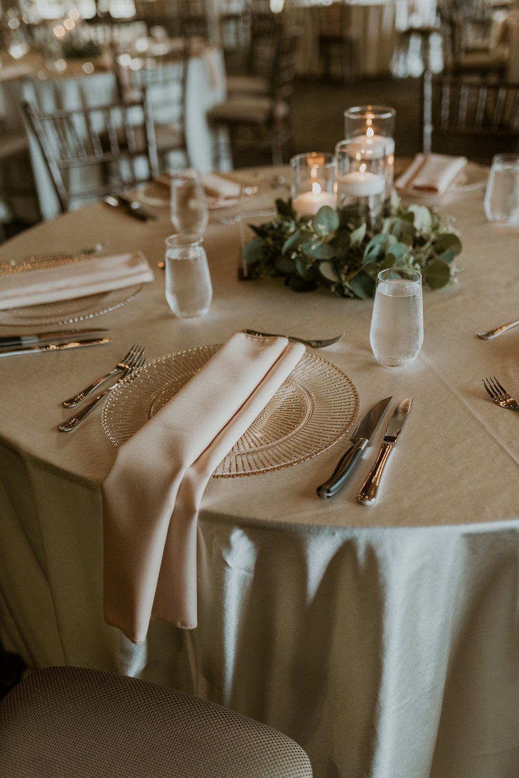 Table setting with white linen and plates decorated with roses and greenery centerpieces.
