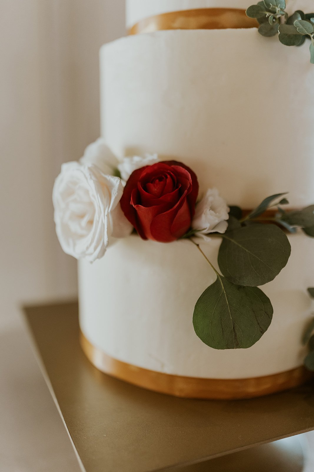 Simple modern cake decorated in white roses with a single red rose and greenery.
