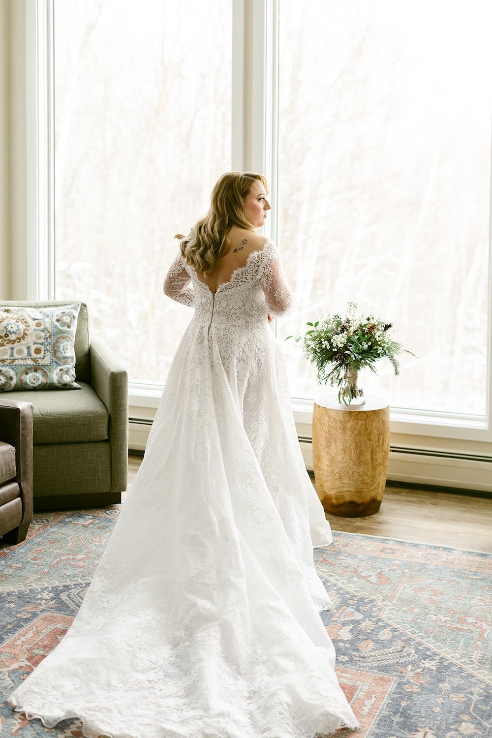 The bride admires her view as her gorgeous lace wedding gown decorates the floor.