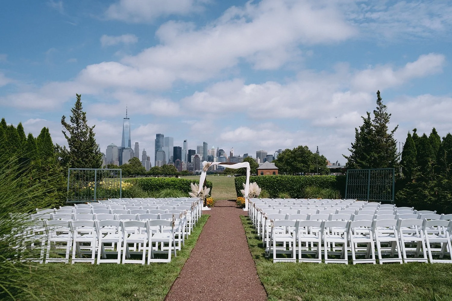 View of the wedding ceremony location. White chairs and archway decorated in their wedding floors. New York City buildings stand in the background. 