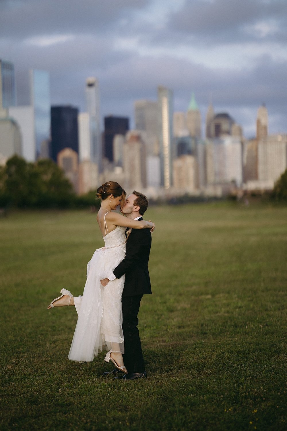 The groom holds his bride up as she kicks her leg out. The couple have New York City scape as their background. 