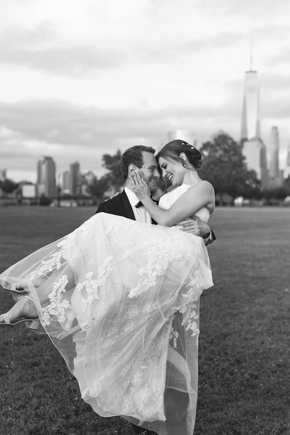 Black and white photo of the groom is carying his bride as she holds her head close to his. 