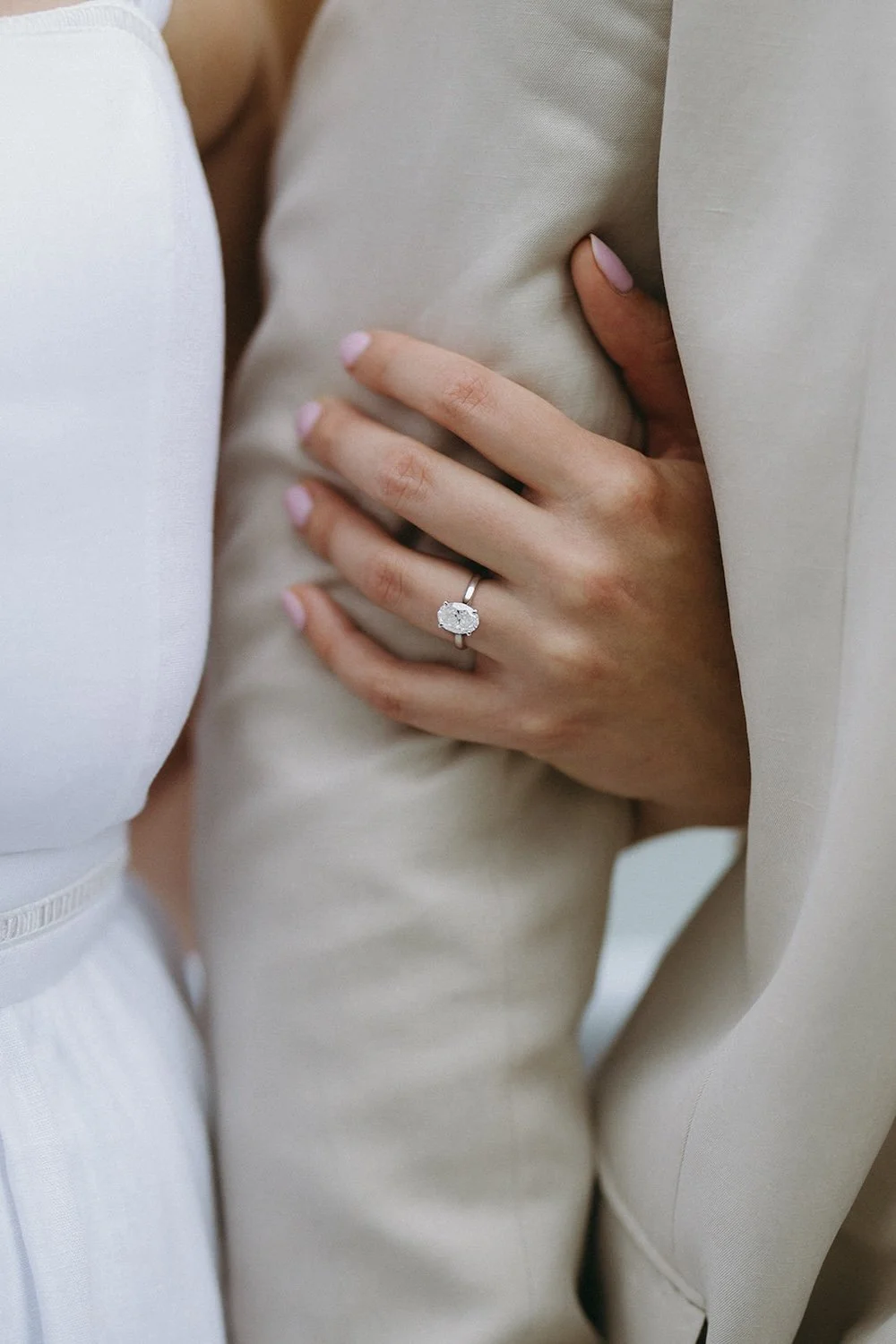 The bride wraps her hand around her future grooms arm. Wedding band shines within the photo. 