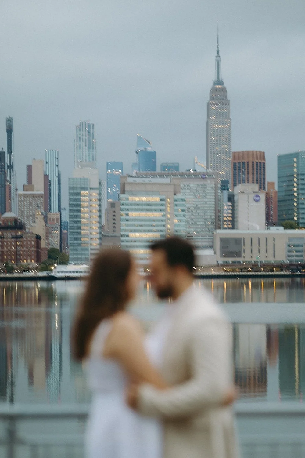 Blurred photo of the couple holding one another close with the city scape in the background. 