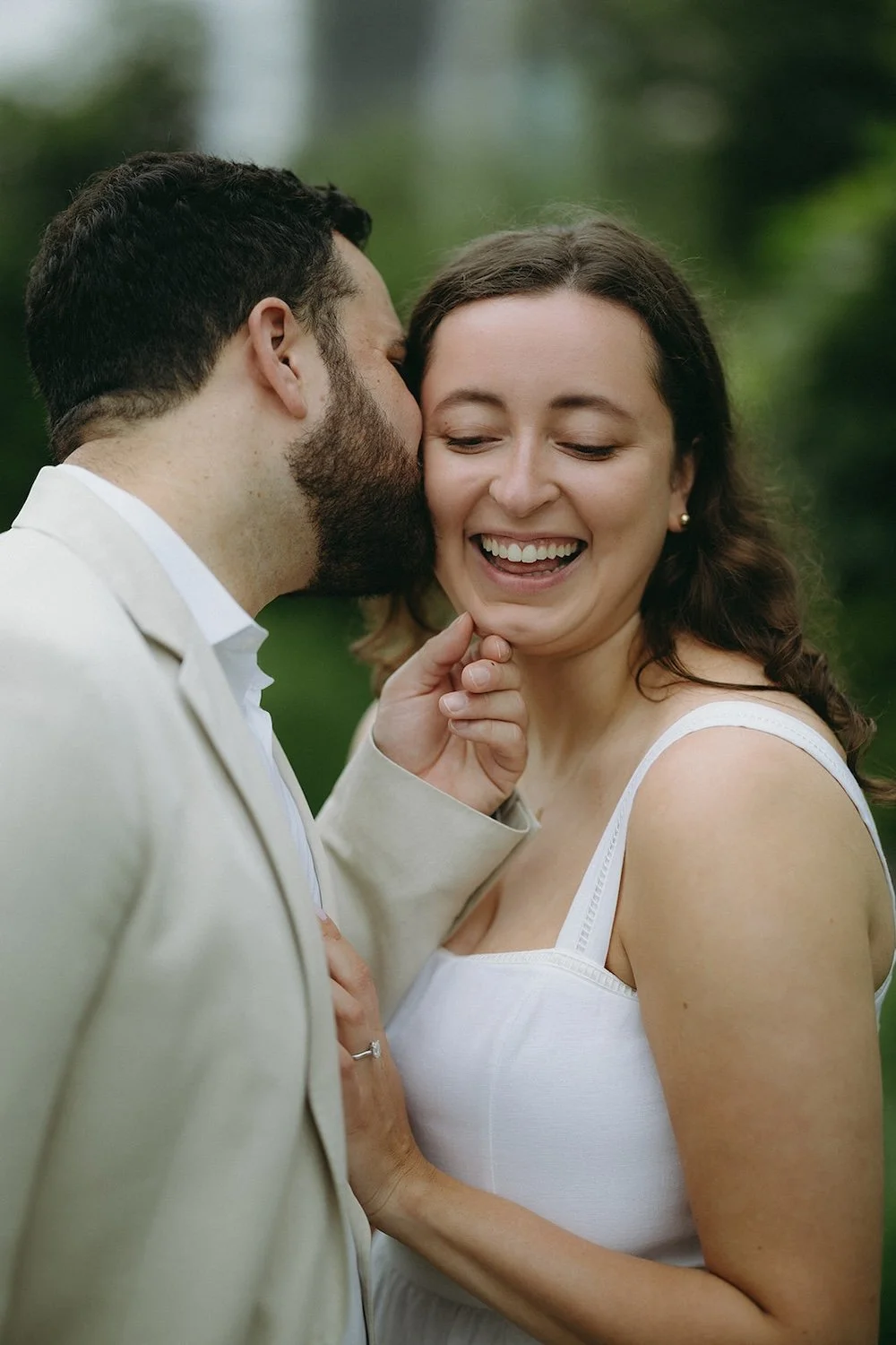 Future groom holds his bride to be by the chin while leaving a kiss on her cheek. 