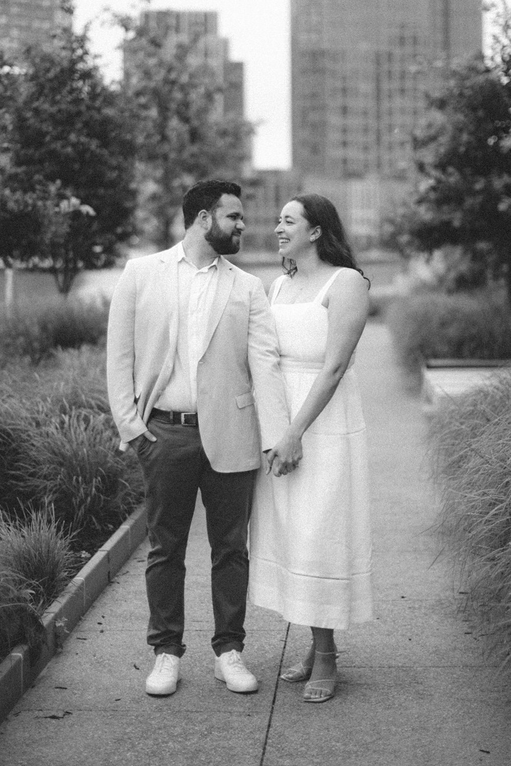 Black and white photo of the couple standing side by side holding hands. 