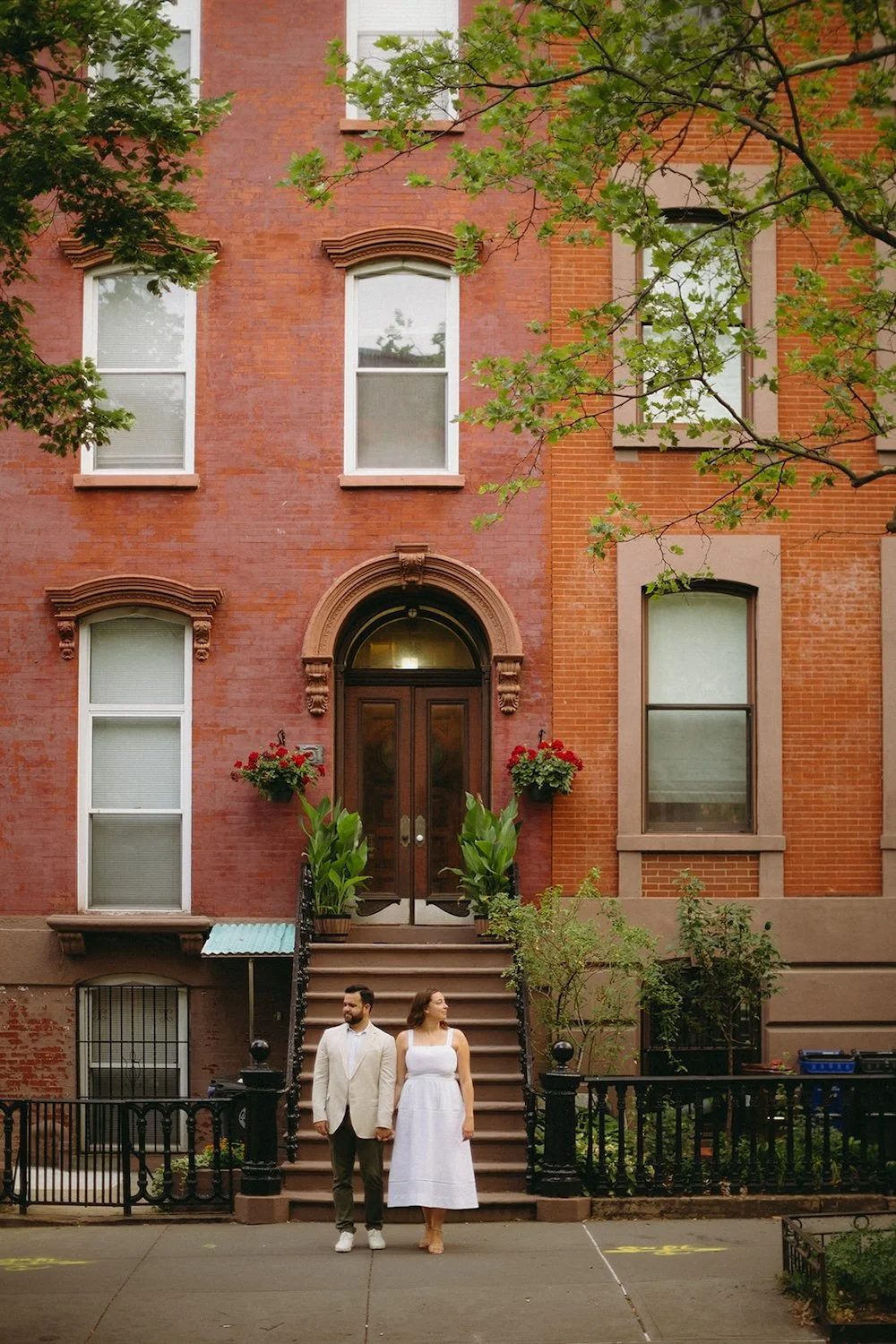 The couple stand infront of the stairs watching the cars pass by. 