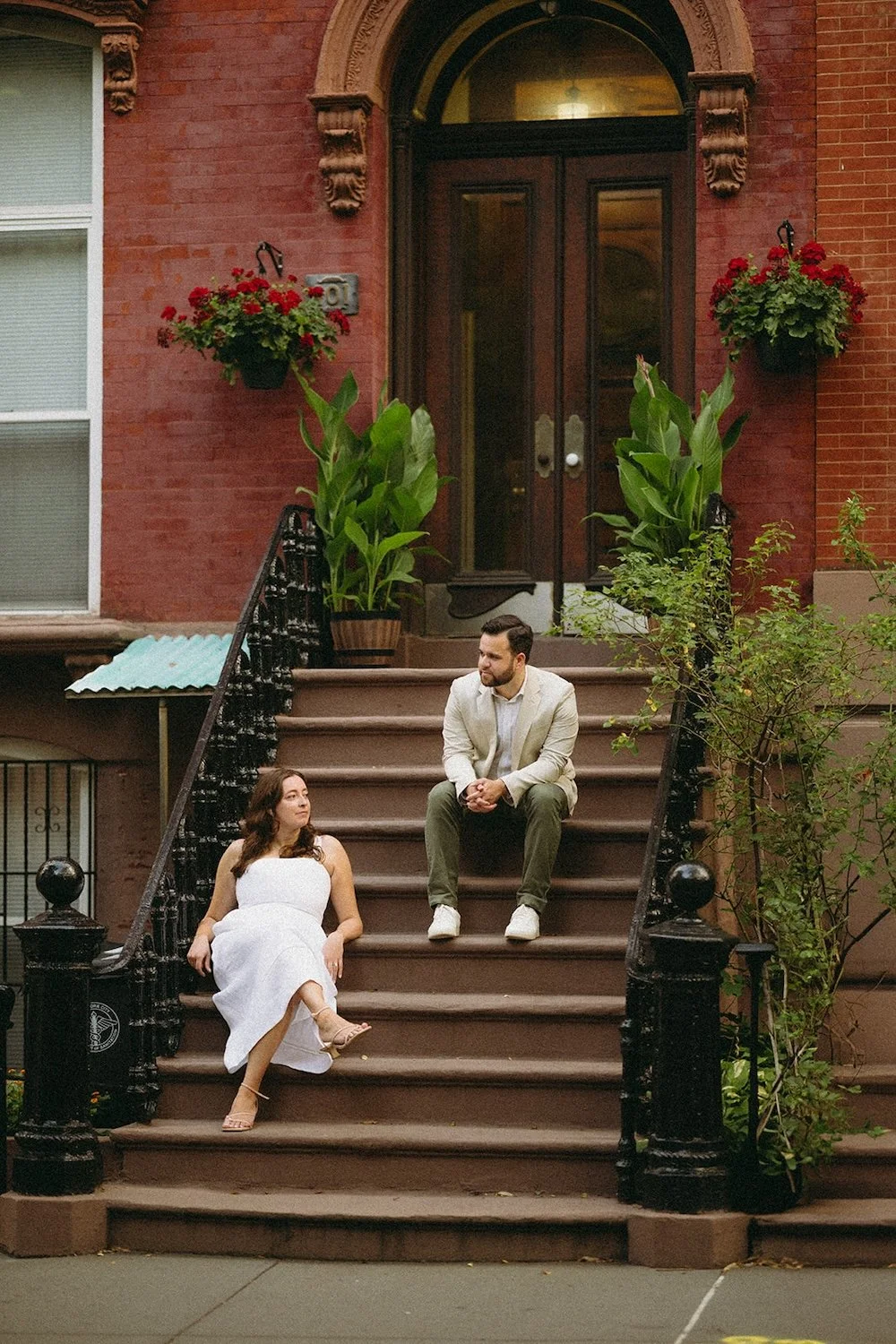 The couple relax on the steps of a brown-stone building. 
