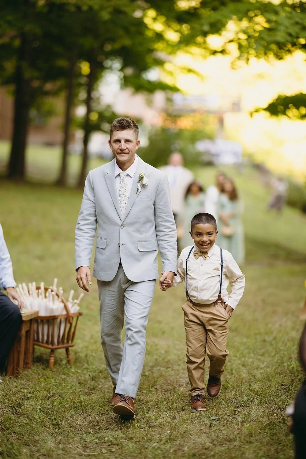 The groom walks down the aisle with ring bearer. 