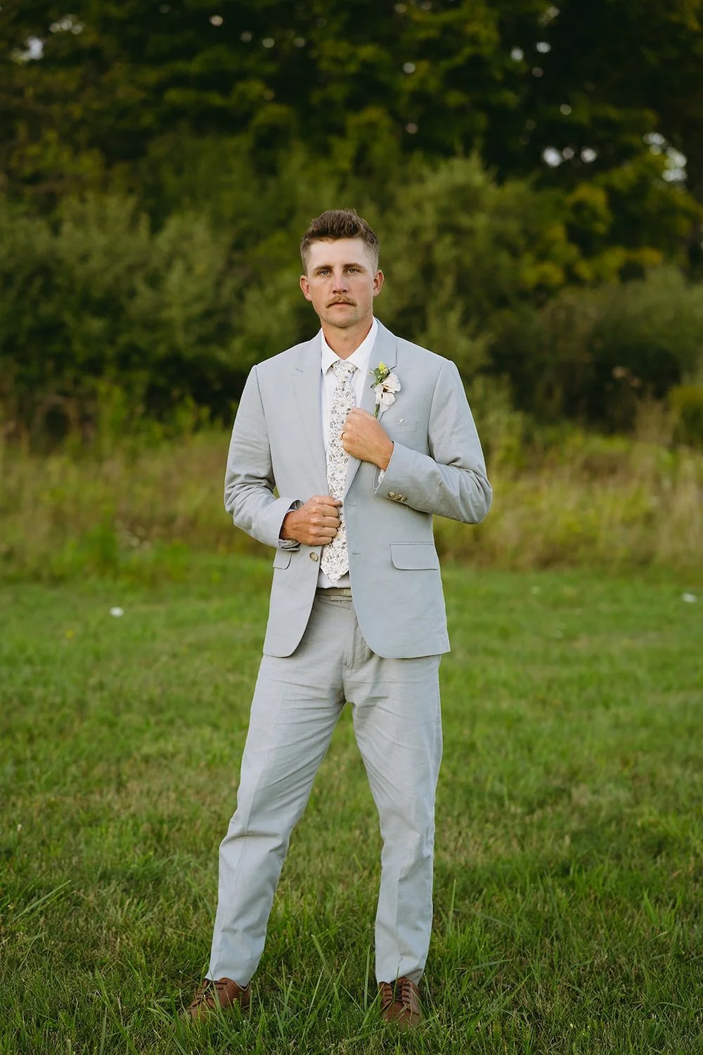 The groom stands posing in his suit. 