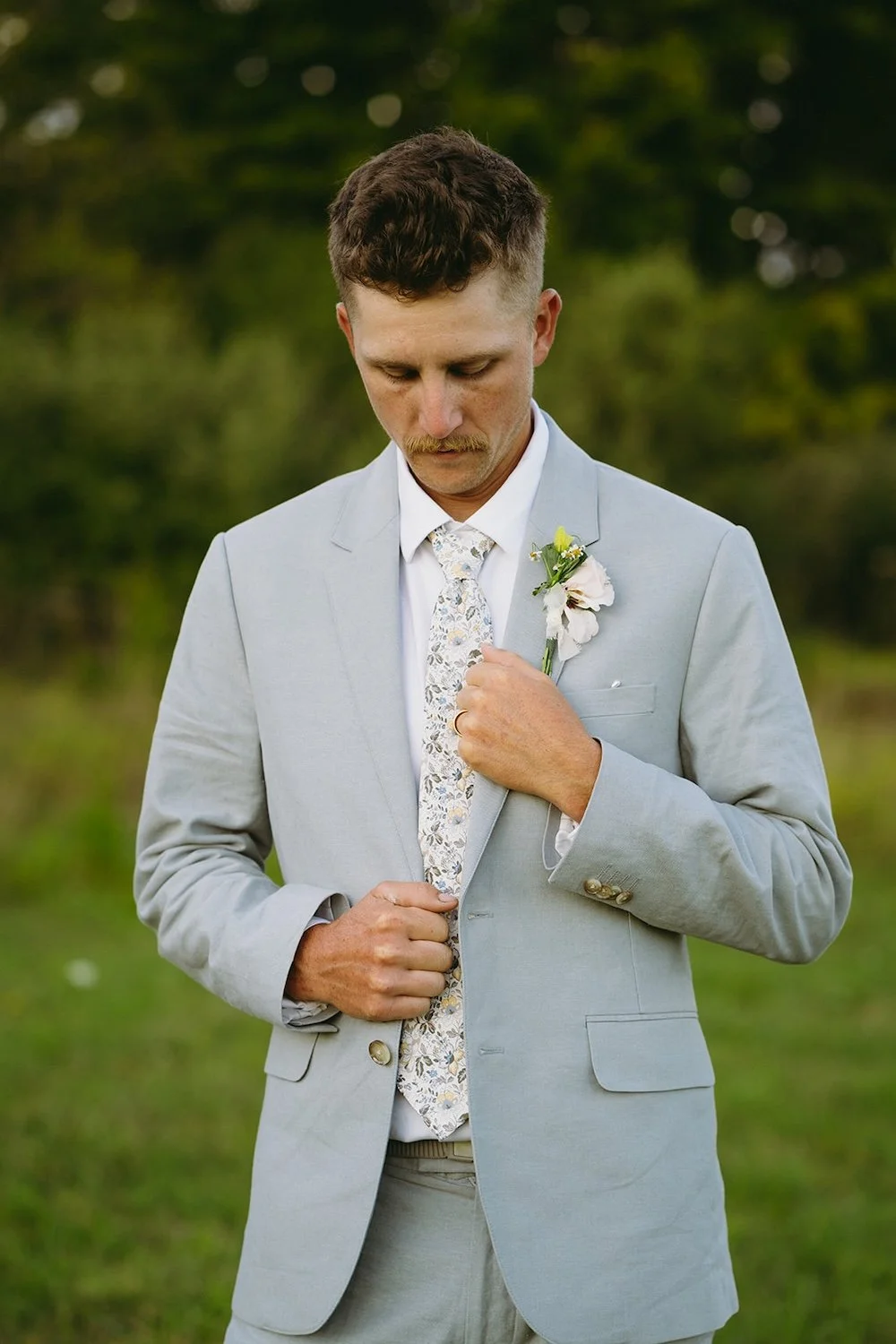 The groom stands holding his suite as he looks down.