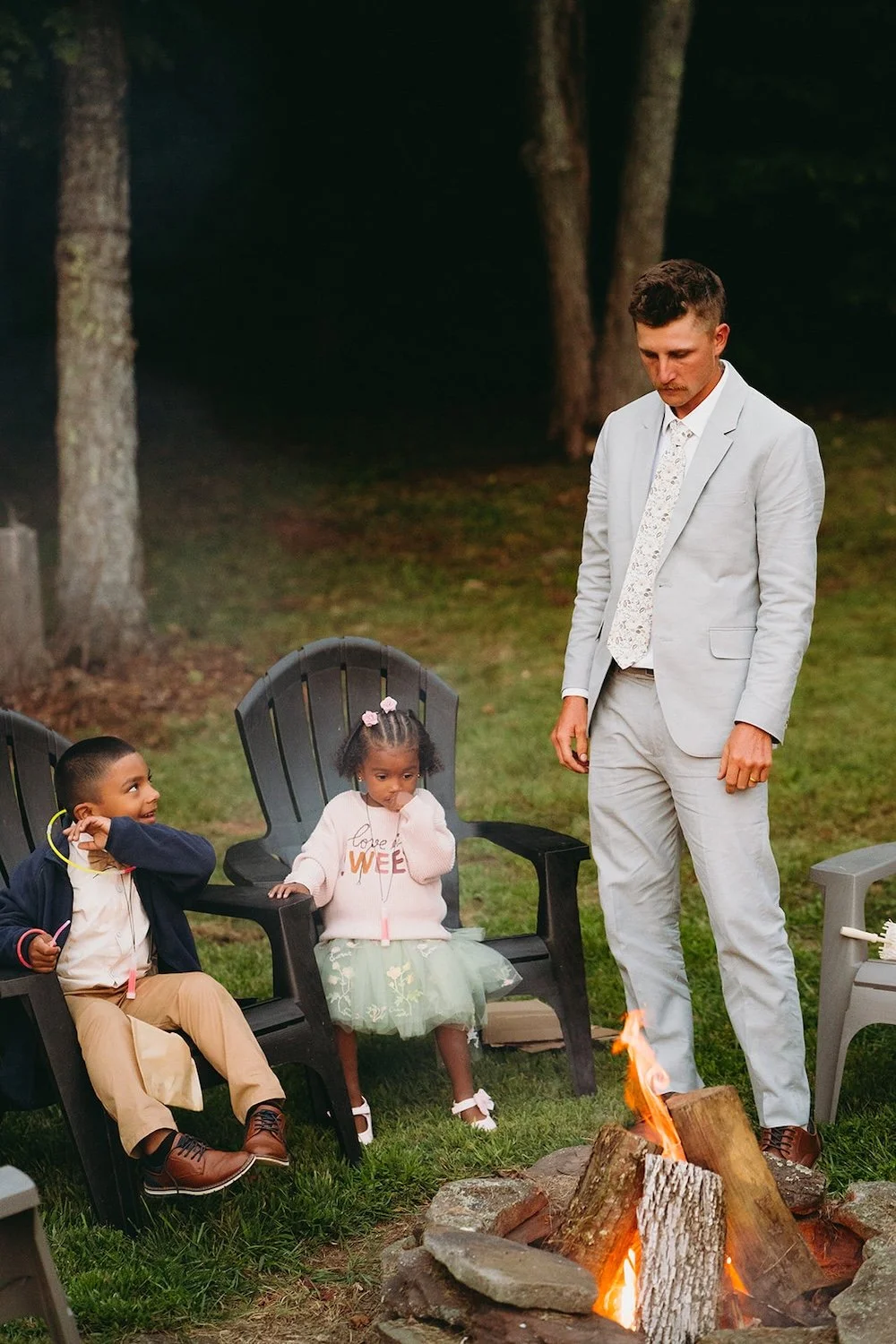 The groom stands at the fire with the kids at the wedding. 