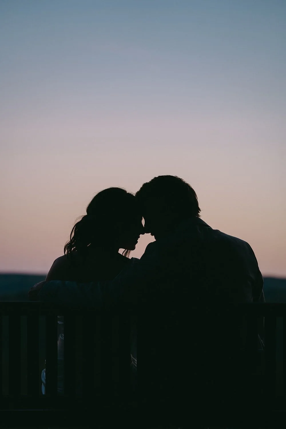 The bride and groom pose for a silhouette photo during blue hour. 