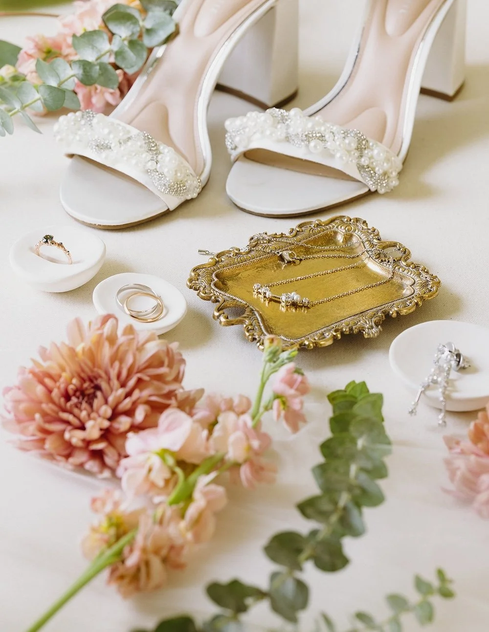 Detail photo of the brides wedding shoes, rings and florals. 