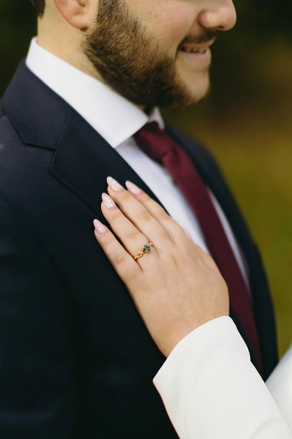 Close up view of the brides engagement ring on the brides hand against the grooms chest. 
