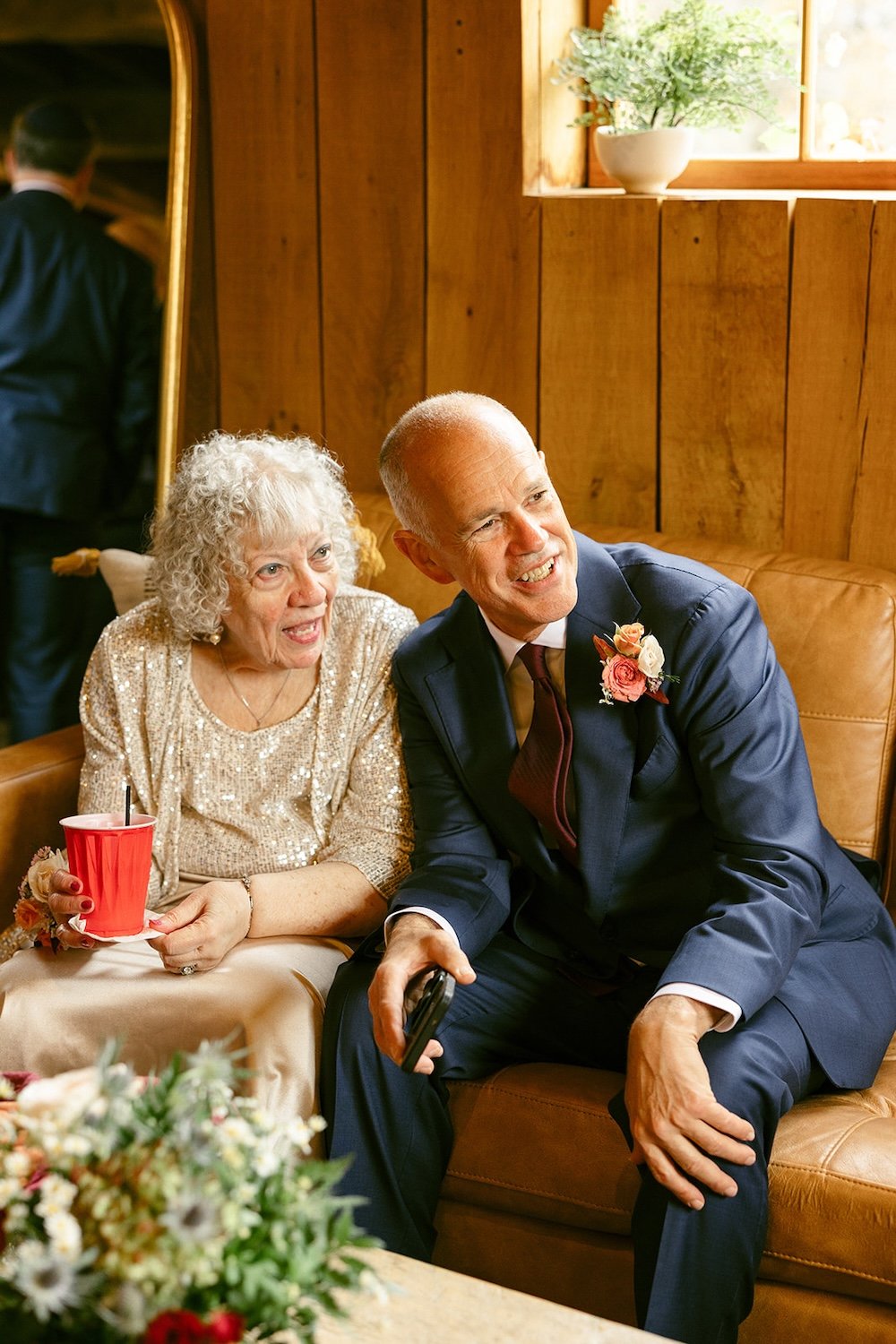 Family sit on the couch observing other guests at the wedding. 