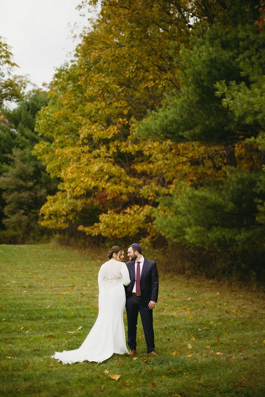 The bride and groom stand together posing with her back to the camera. Her gown fanned out as the groom admires her from the side. 