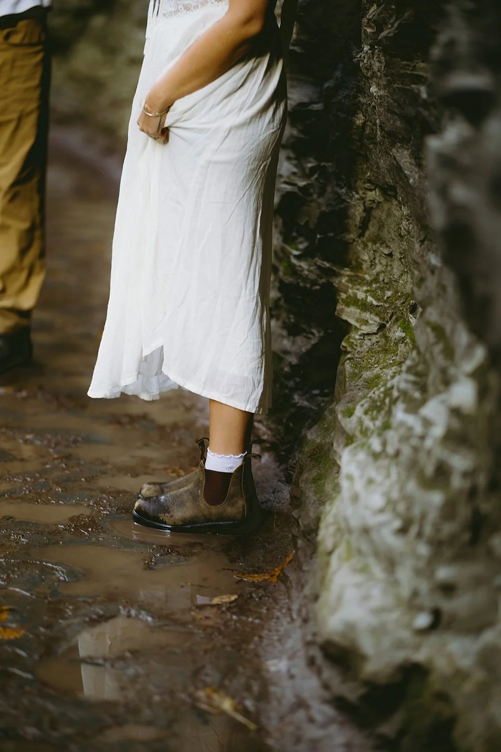 Detail photo of the brides boots and bottom of her dress standing in a puddle. 