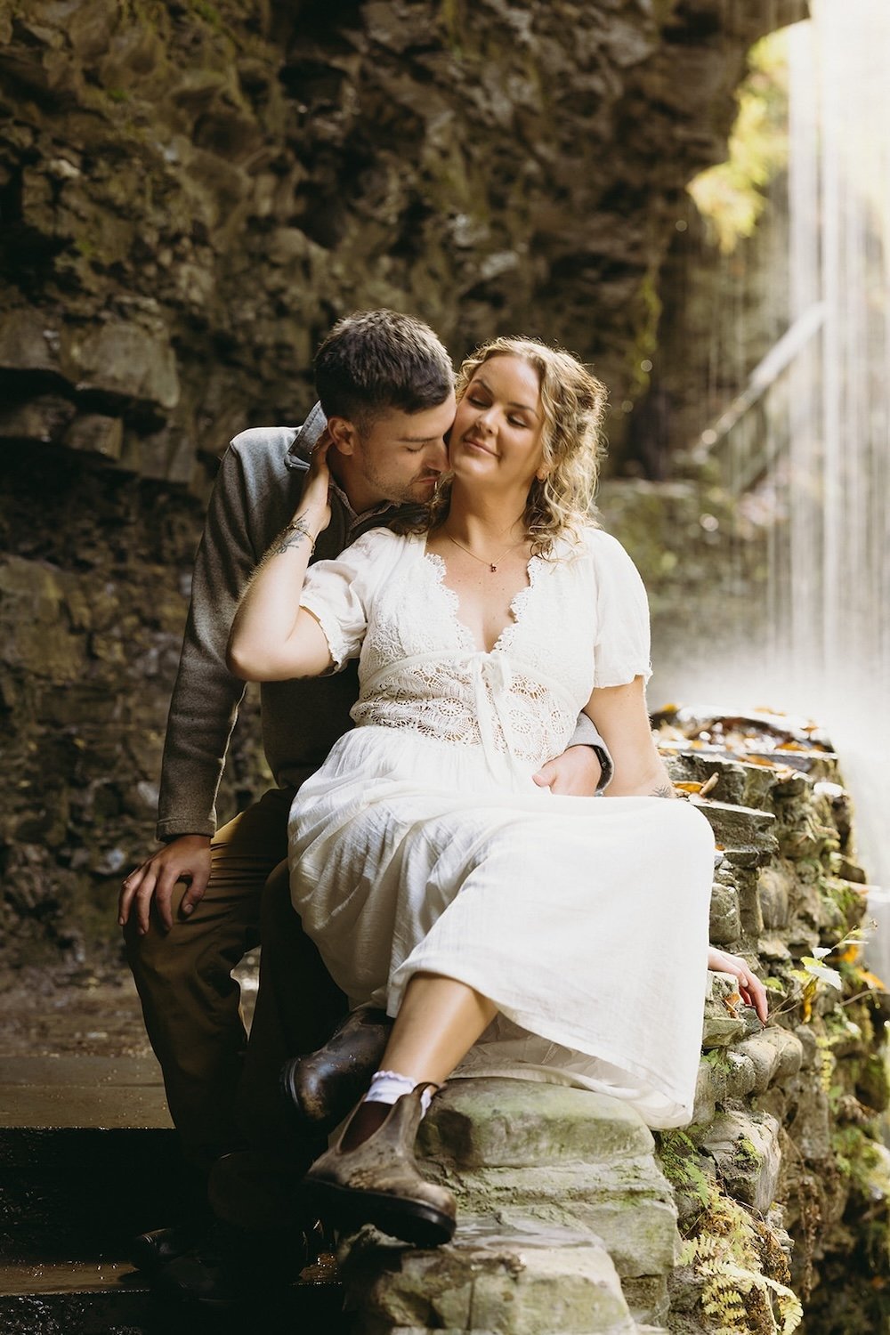 The future groom nestles his head into his future brides neck as they rest together on the ledge. 