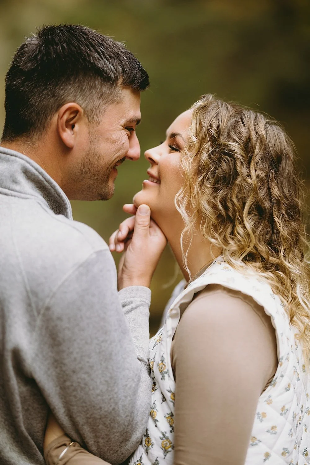 The future groom holds his bride to be's chin as they share a smile together. 