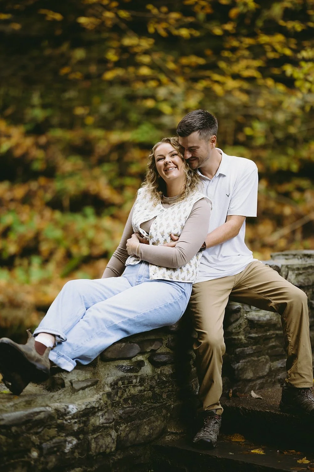 The future bride relaxes on the rocks resting her head on her future grooms chest. 