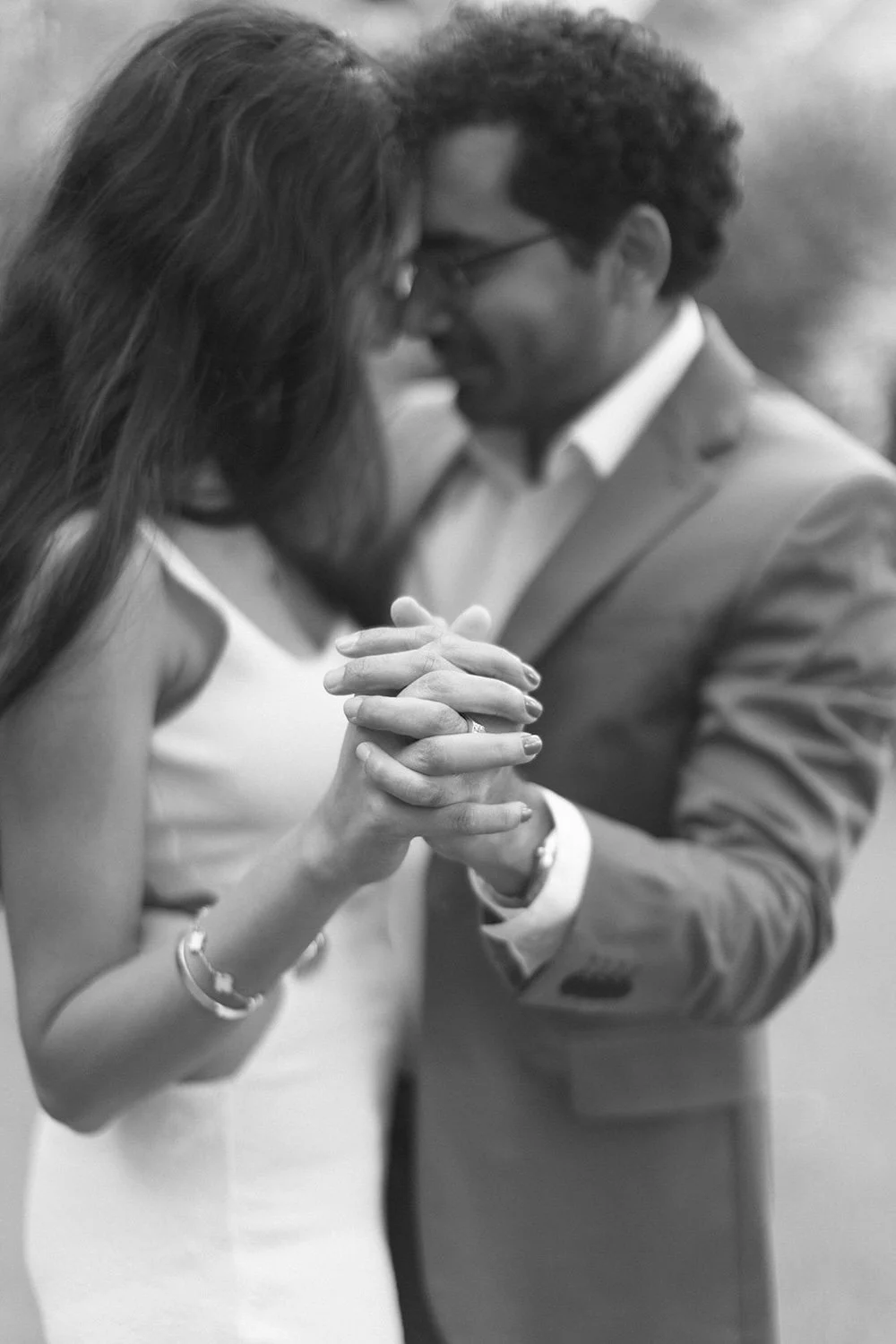 Black and white photo of the couple holding hands while their touch their faces closely. 