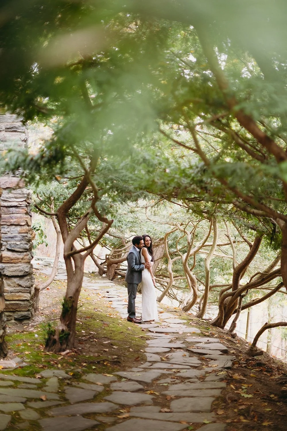 The future groom snuggles his future bride with the trees surrounding them on the pathway. 