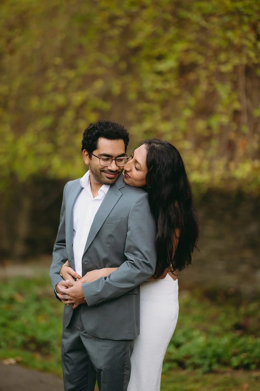 The future bride holds her groom from behind with her arms wrapped around him. 