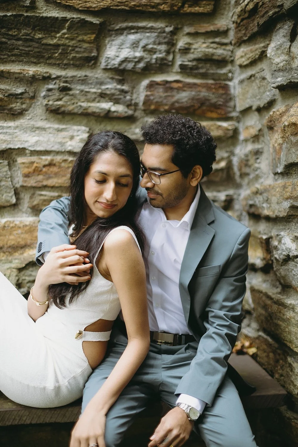 The future bride rests into her future groom with the beautiful brick of the church sits behind them. 